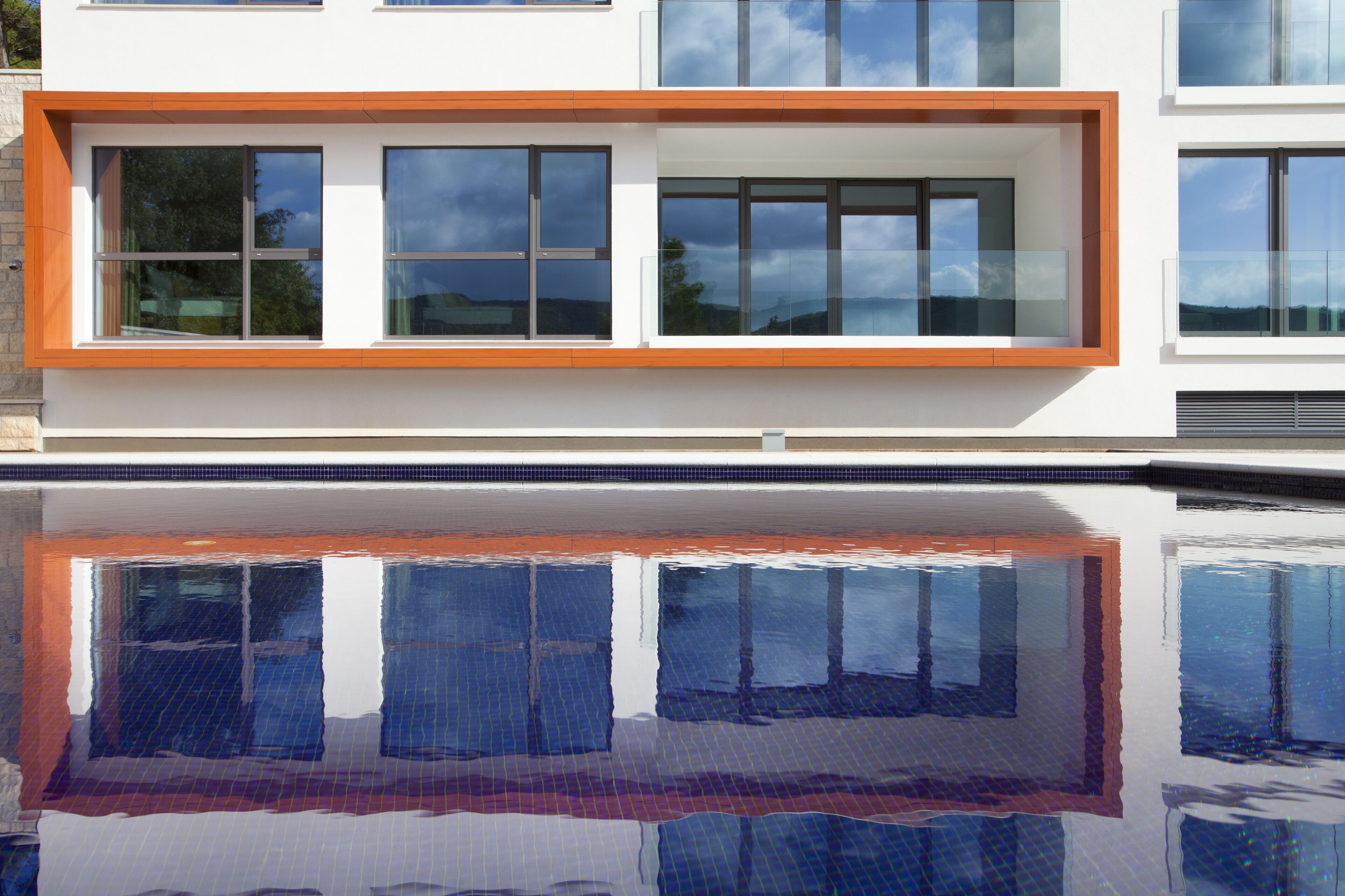 Ein modernes Gebäude mit großen Fenstern und Spiegelung im darunterliegenden Wasser.