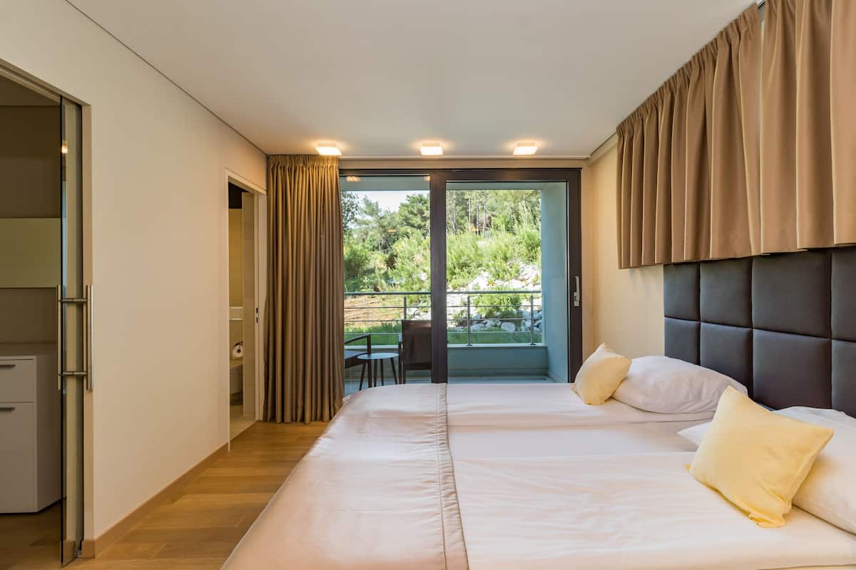 A bedroom with a large bed, a desk, and a view of a balcony with outdoor furniture.