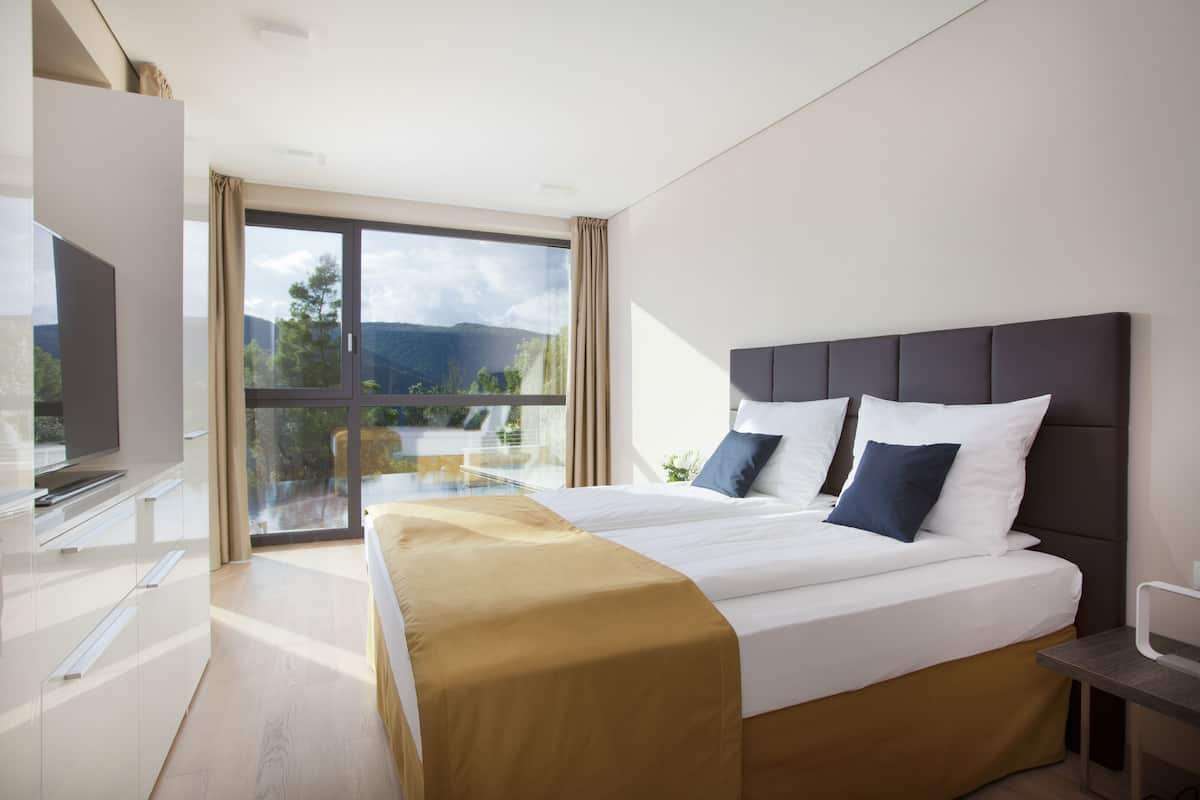 A modern hotel room with a large bed, a television, and a balcony with a scenic view.