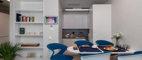 A modern dining area with a round table, blue chairs, and a kitchen in the background.