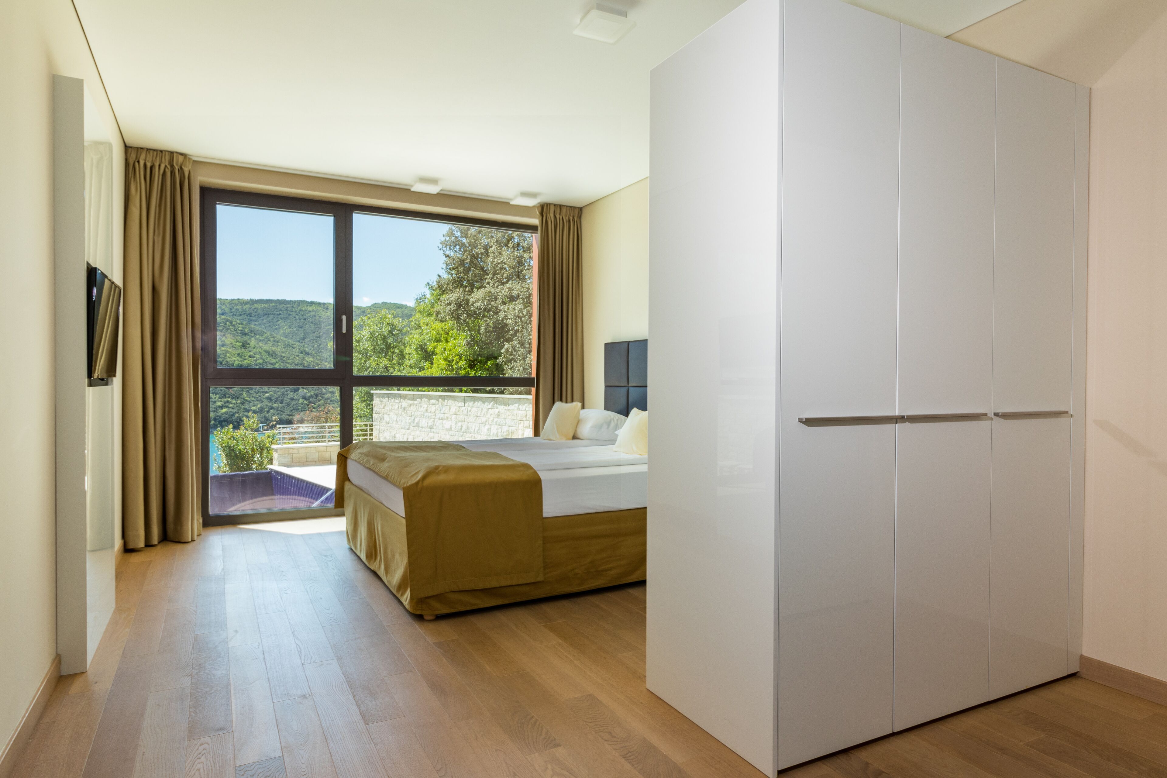 A bedroom with a bed, a wardrobe, and a large window with a view of greenery.