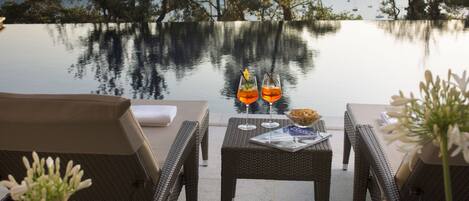 A serene outdoor seating area with wicker furniture and a table set with drinks and a menu, overlooking a calm body of water with boats.