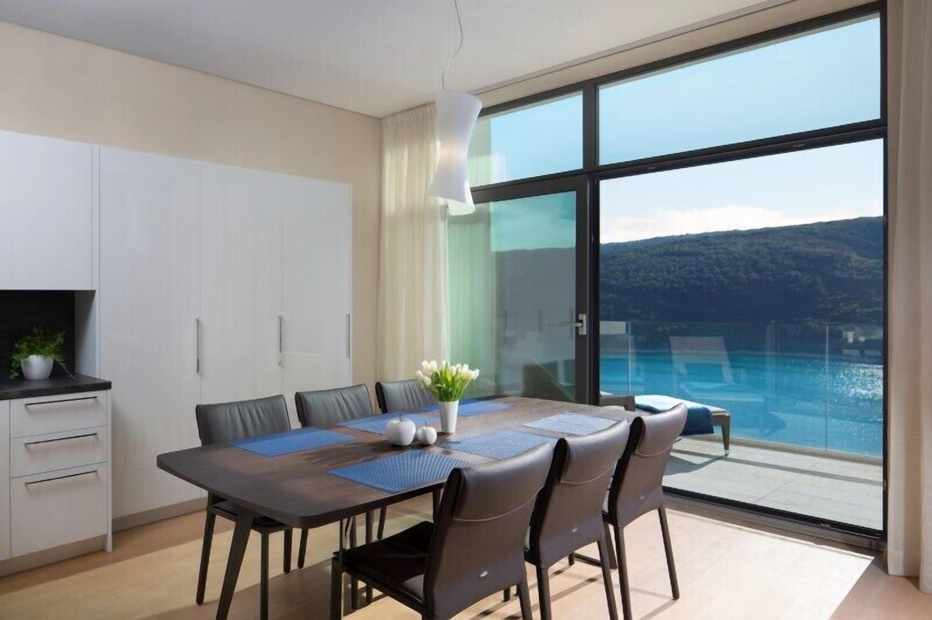 Zona pranzo moderna con un tavolo grande, sedie e vista su una piscina e montagne attraverso ampie finestre.