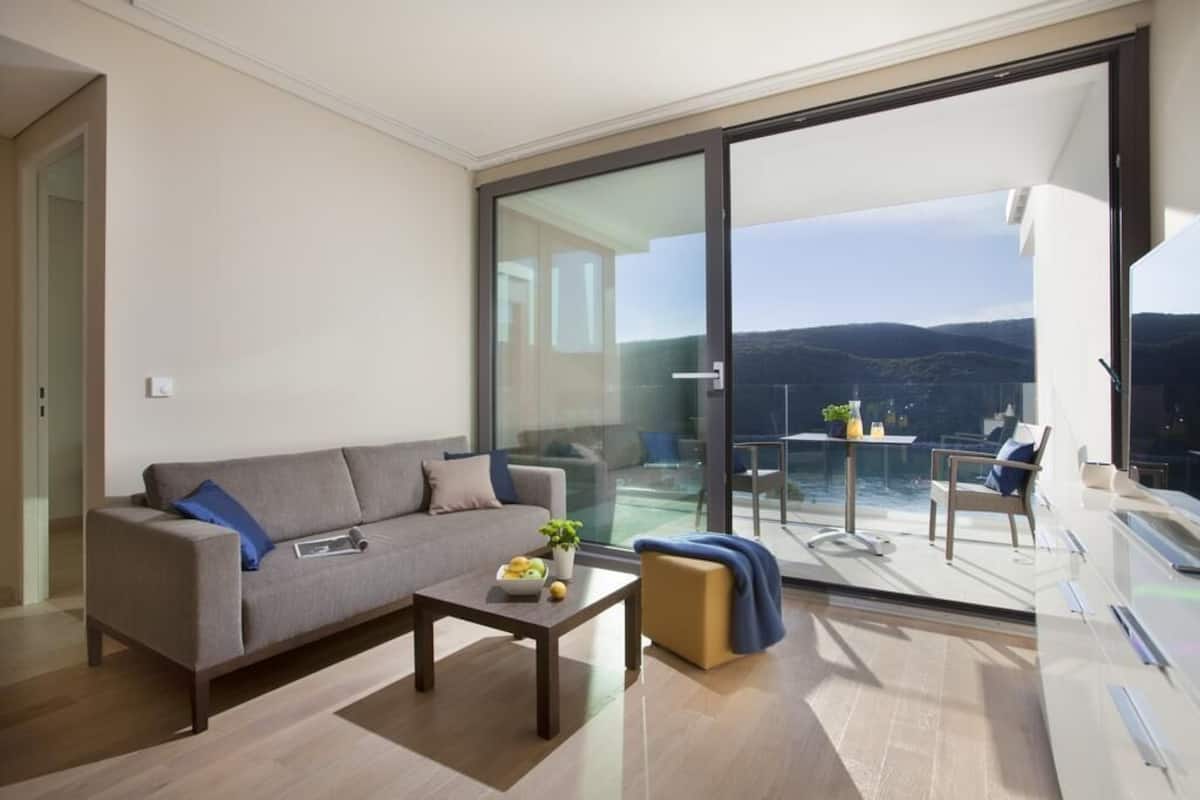 A modern living room with a sofa, coffee table, and a view of a balcony with a pool.