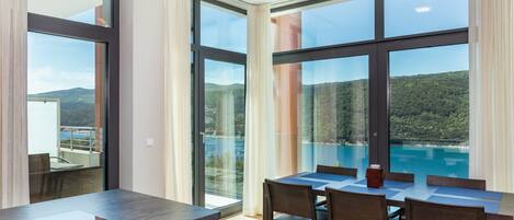 A modern kitchen with a large island, dining area with chairs, and large windows offering a view of a lake and mountains.