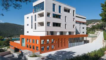 Un edificio moderno de varios pisos con techo plano, grandes ventanales y una combinación de paredes exteriores blancas y anaranjadas.