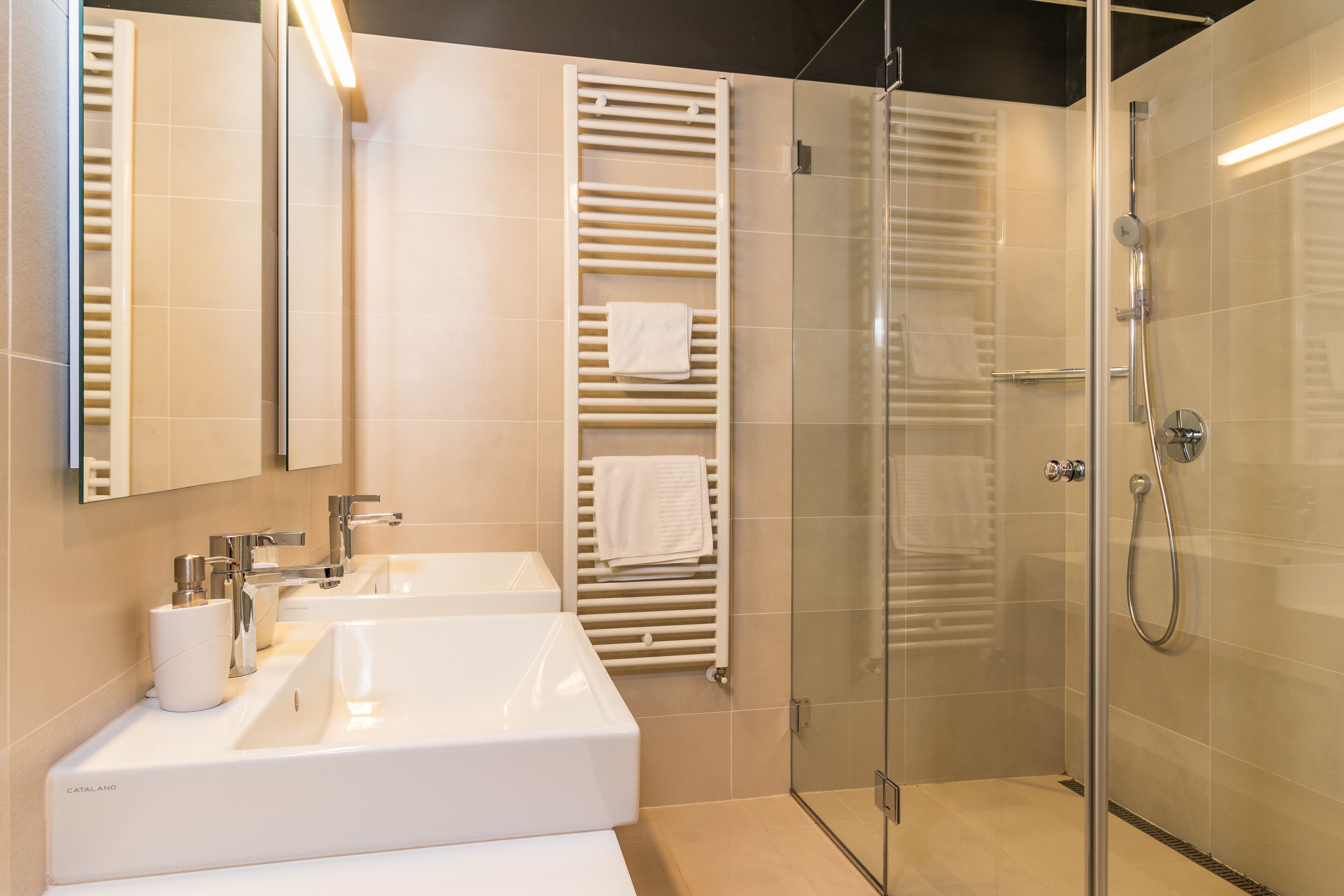 Une salle de bain moderne avec deux vasques, une douche en verre et un porte-serviettes.