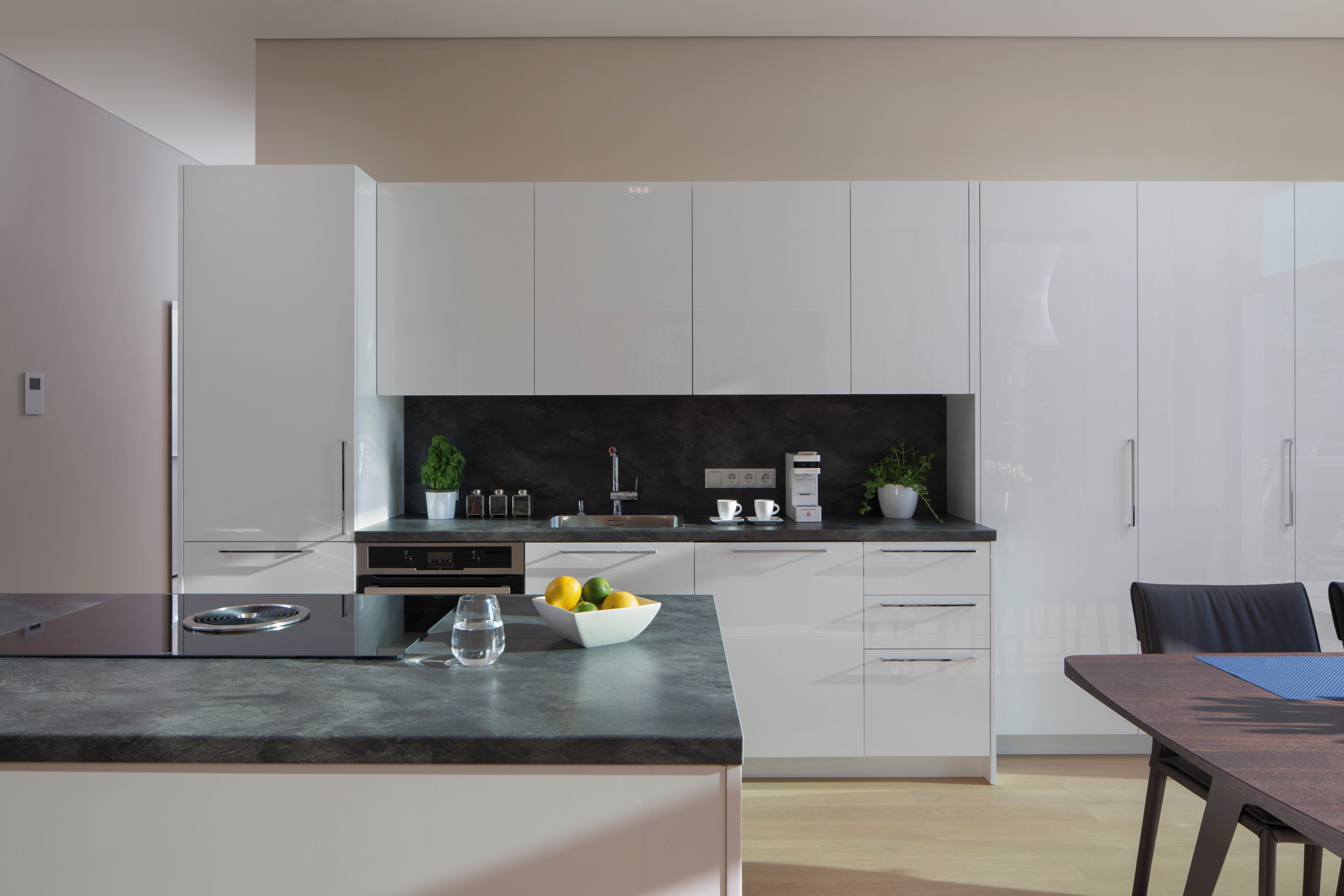 A modern kitchen with white cabinets, a black countertop, and a dining area with a table and chairs.
