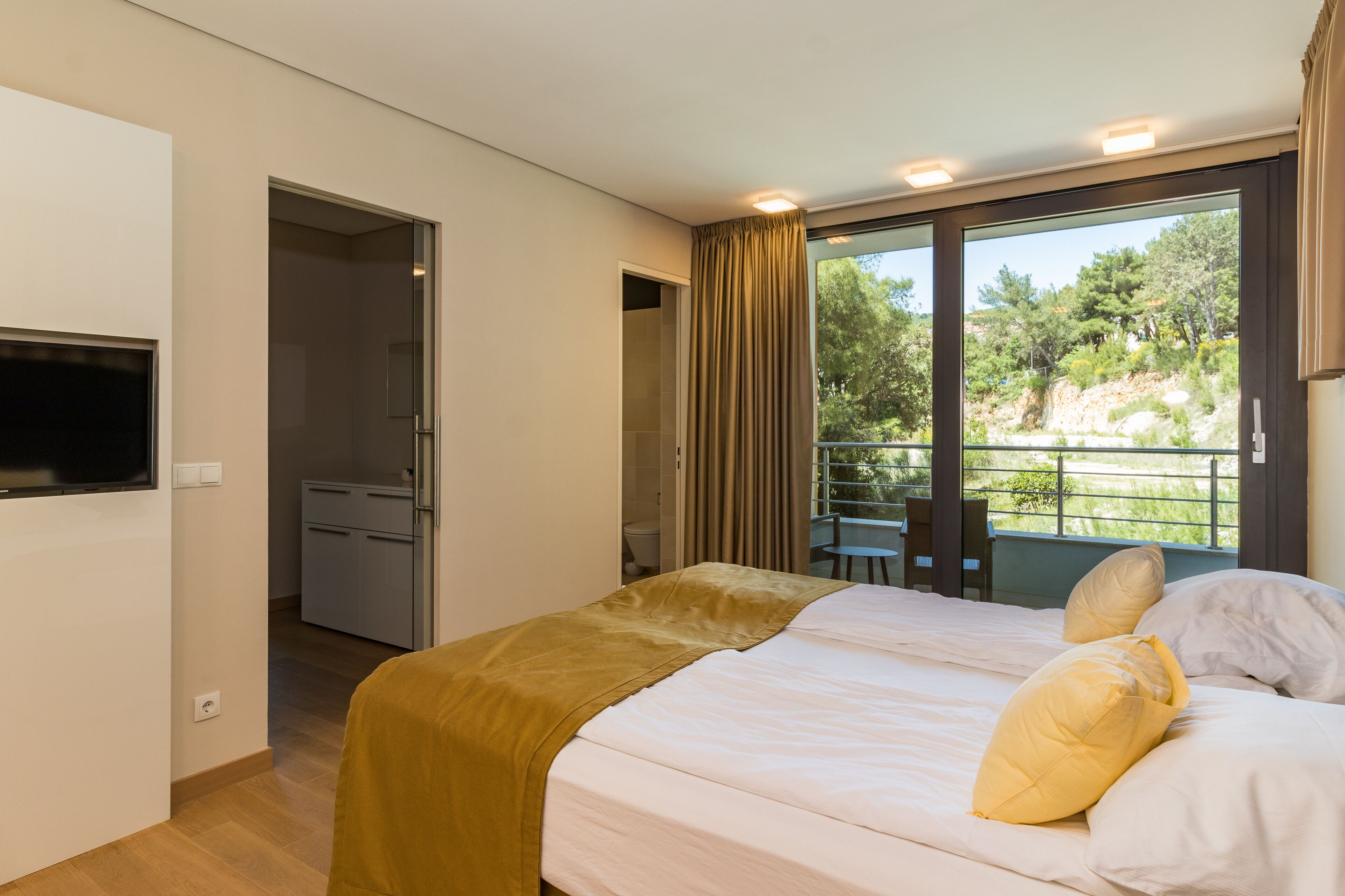 Une chambre à coucher avec un lit, un téléviseur fixé au mur et un balcon équipé d’une table et de chaises.