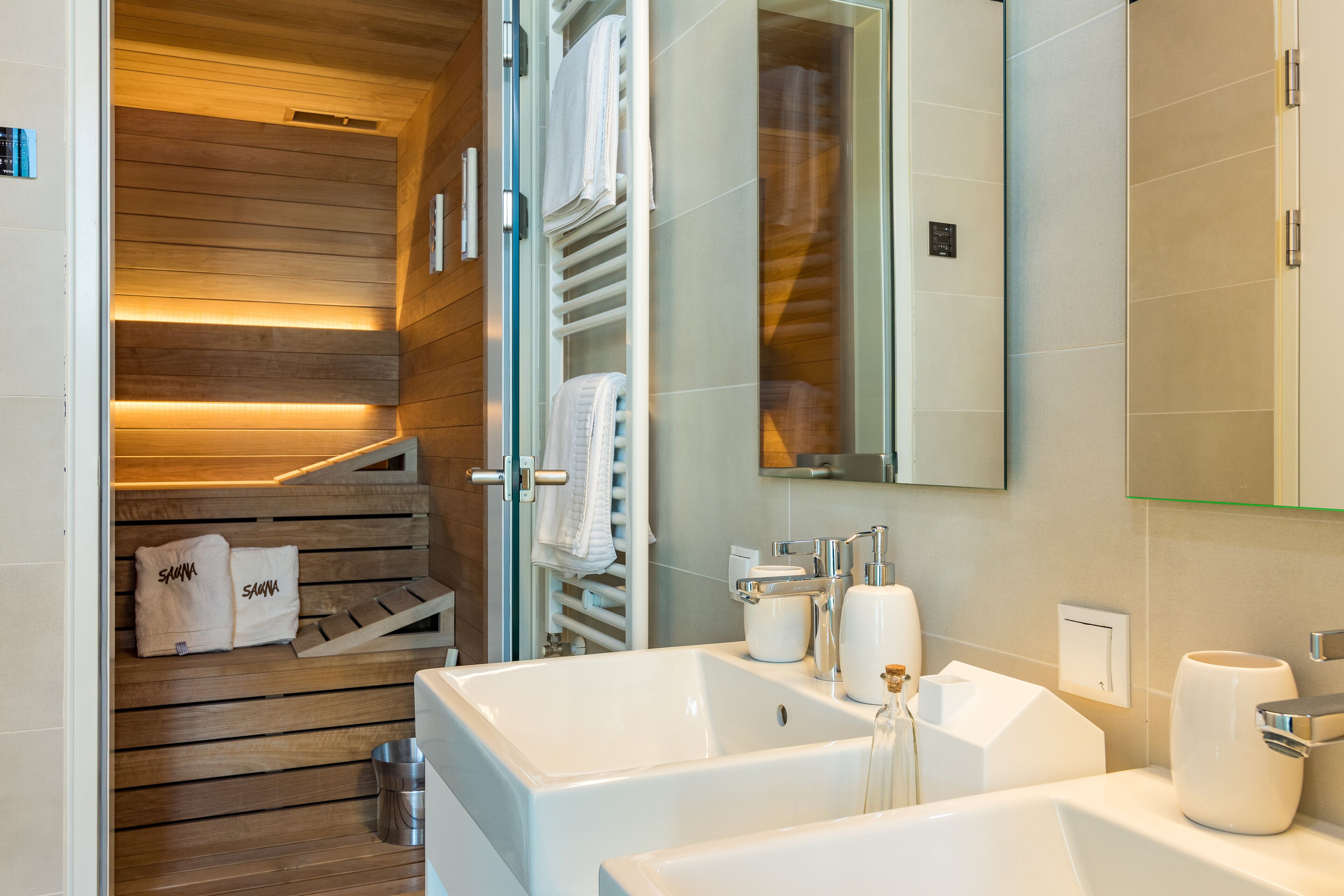 Ein modernes Badezimmer mit einem Holz-Saunabereich, einem großen weißen Waschbecken und einem Spiegel.