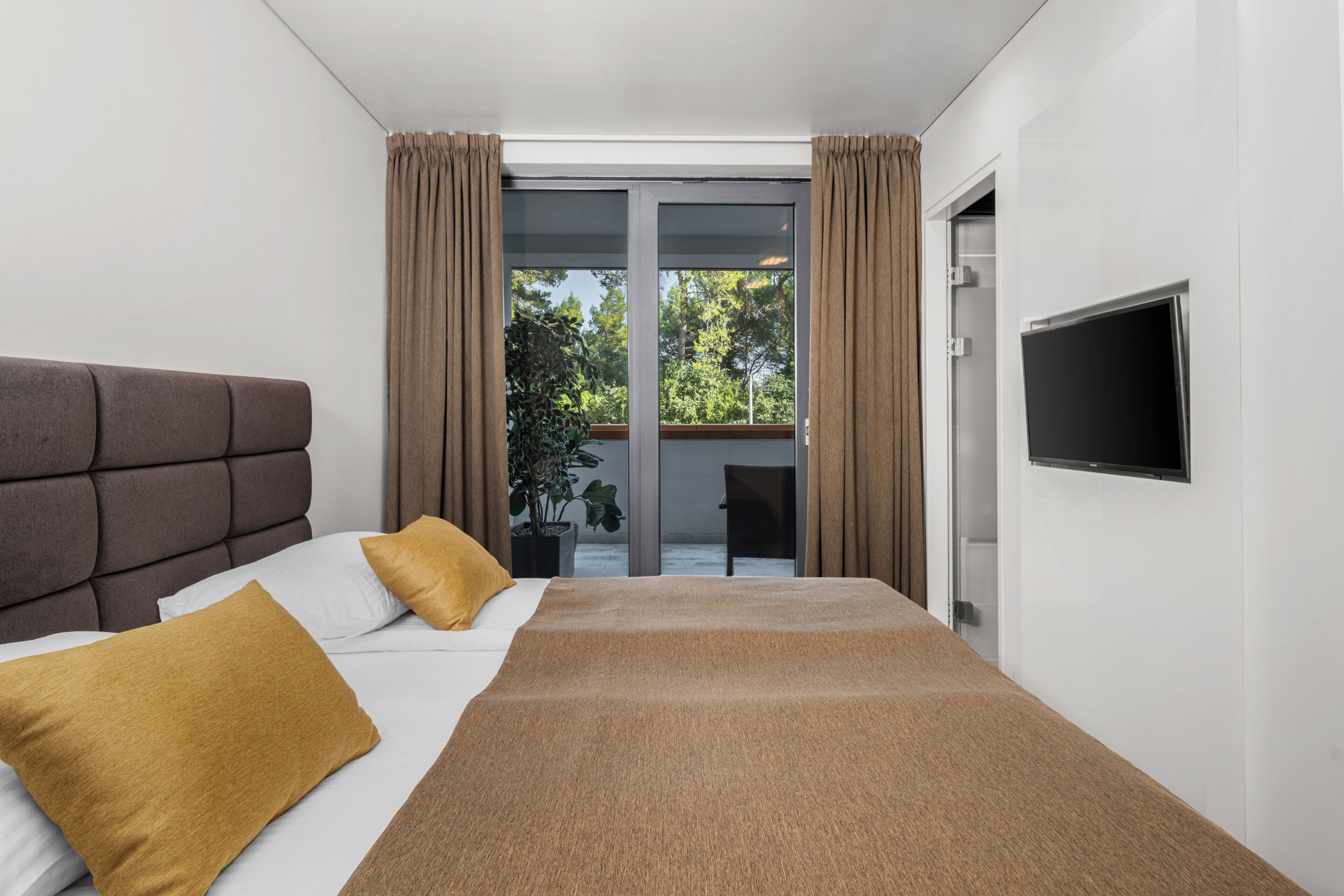 Une chambre d’hôtel moderne dotée d’un grand lit, d’un téléviseur à écran plat et d’une porte-fenêtre coulissante donnant sur un espace extérieur.