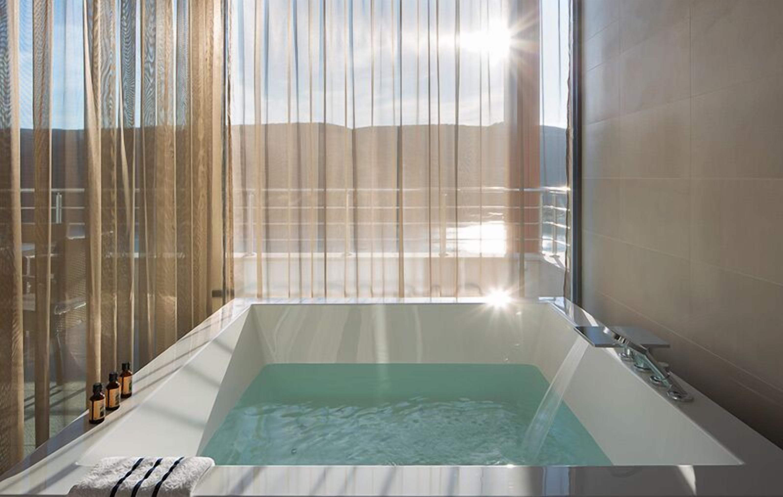 A modern bathroom with a large bathtub, a glass shower enclosure, and a view of the outdoors.