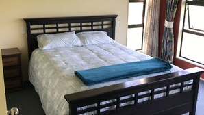 Een slaapkamer met een groot bed, nachtkastje, dressoir en een raam met gordijnen.
