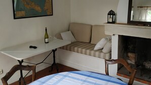 Ett mysigt rum med ett matbord, en soffa, en karta på väggen, en öppen spis och ett runt bord med en rutig duk.