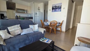 Een woonkamer met een bank, een salontafel en een eethoek met een tafel en stoelen. Achtergrond zichtbaar is een keuken.