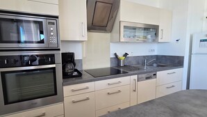 Een moderne keuken met roestvrijstalen apparatuur, waaronder een dubbele oven, magnetron en koffiezetapparaat. Er is een spoelbak met een moderne kraan, en de kastjes zijn licht van kleur.