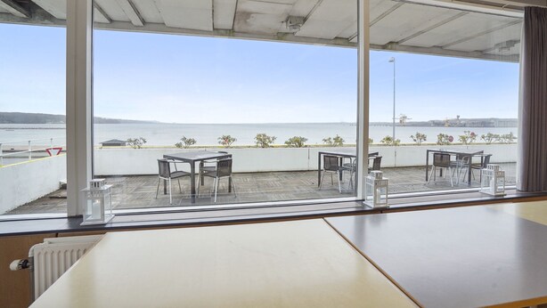 Una habitación con un ventanal grande que da a una terraza con mobiliario exterior y vistas al mar.