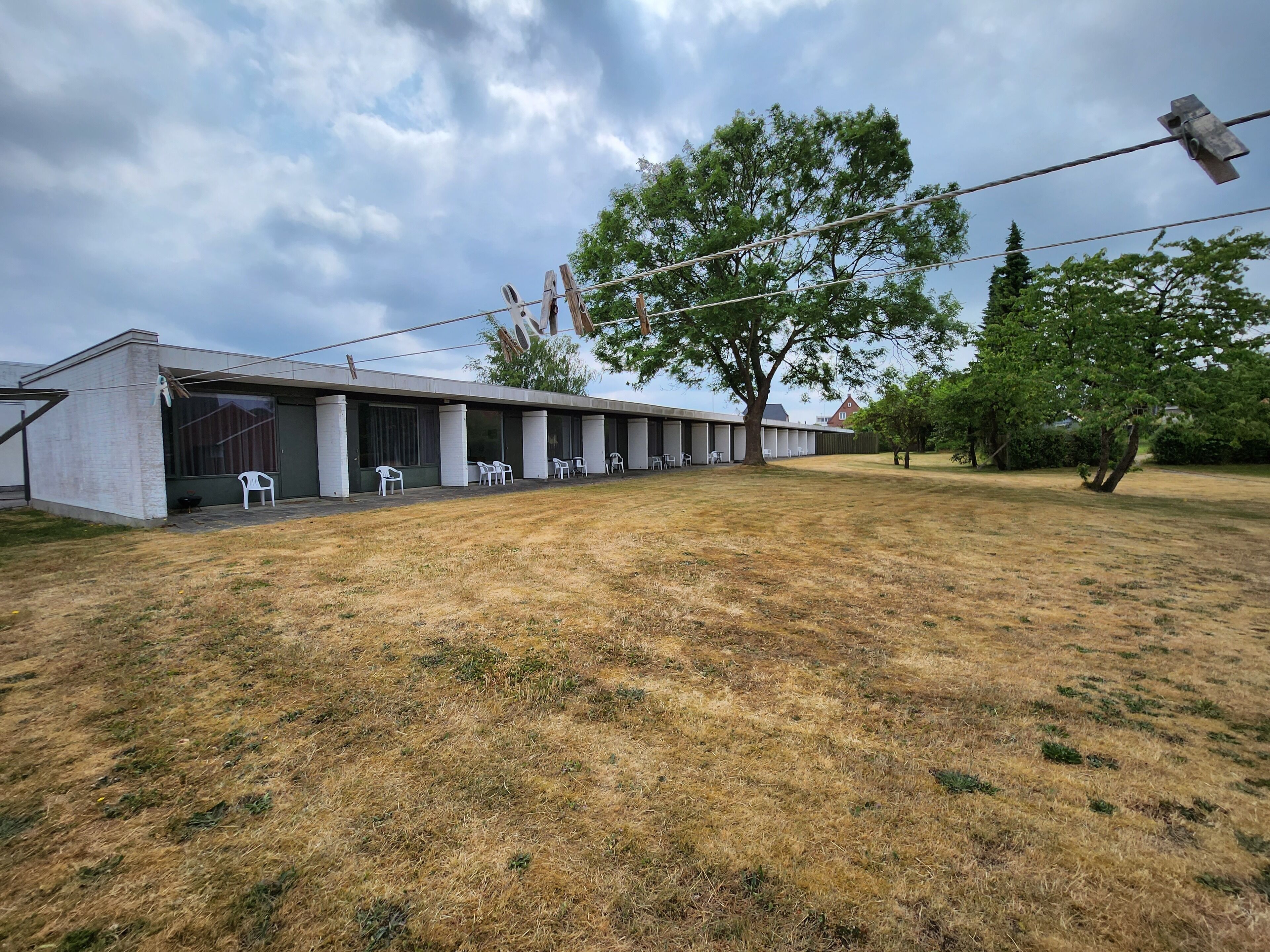 Un edificio moderno con techo plano, ventanas amplias y una zona de estar al aire libre techada con sillas.