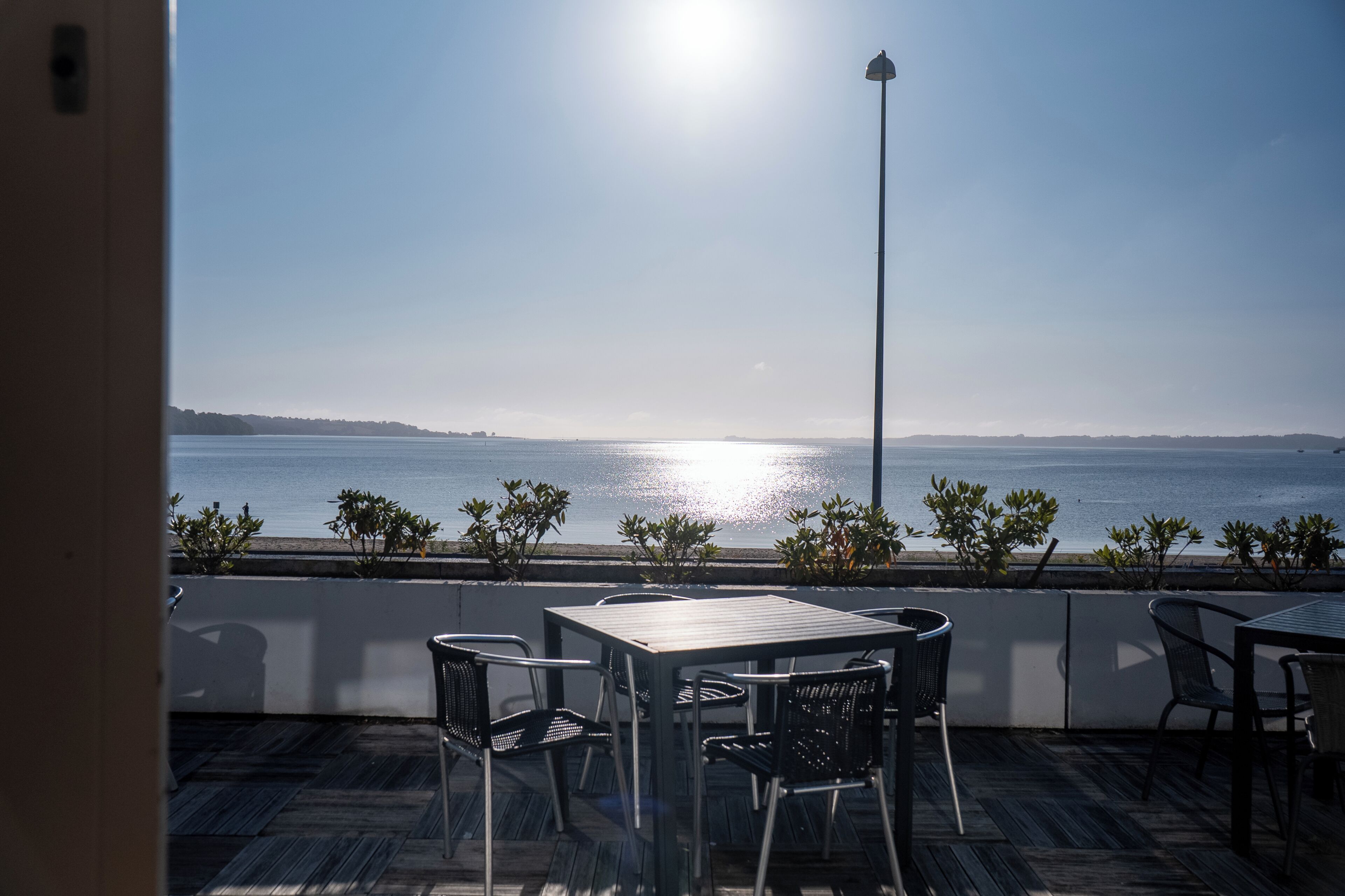 A terrace with a view of the sea, featuring outdoor seating and a street lamp.