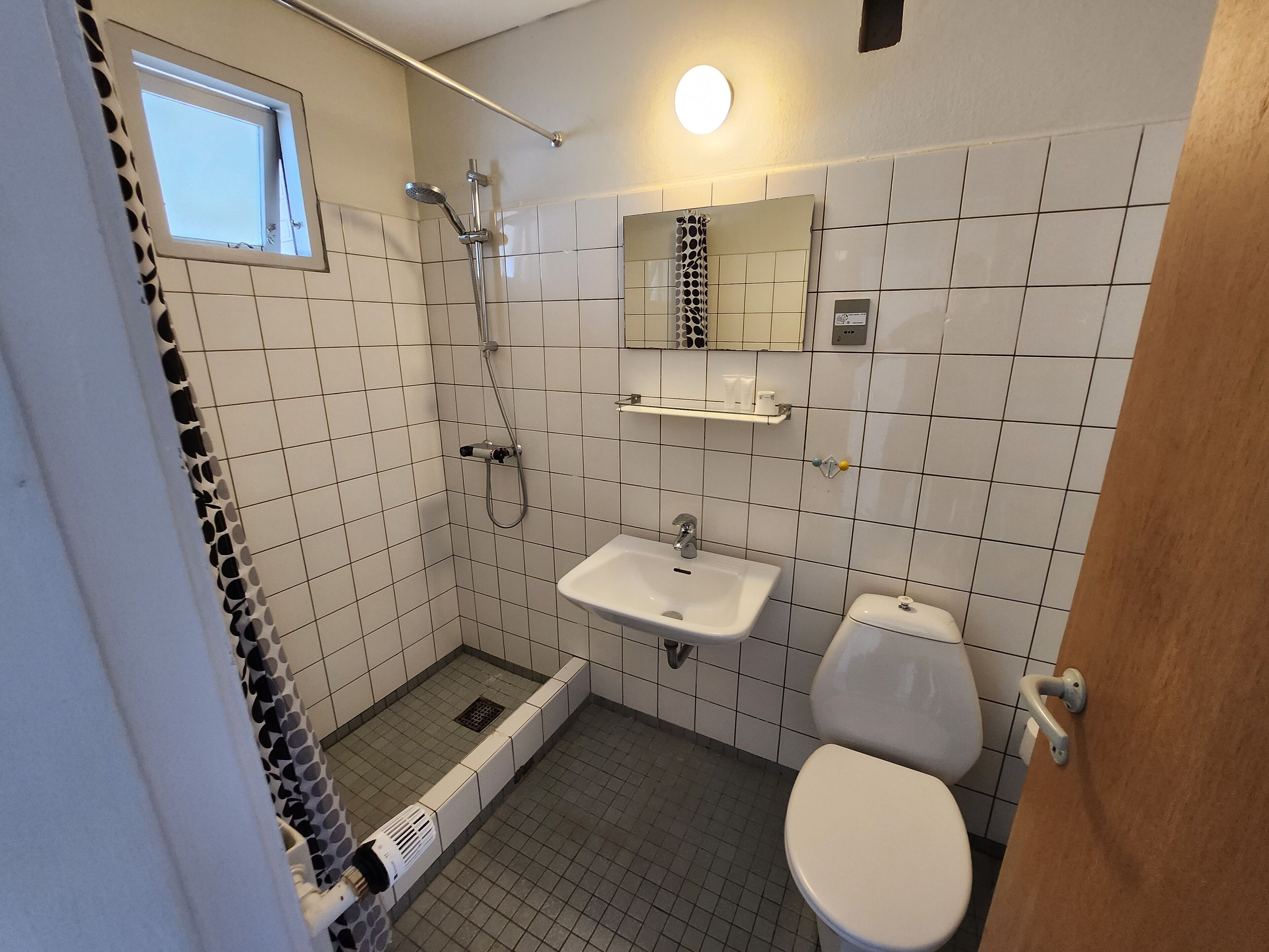 A bathroom with a shower, toilet, sink, and a window.