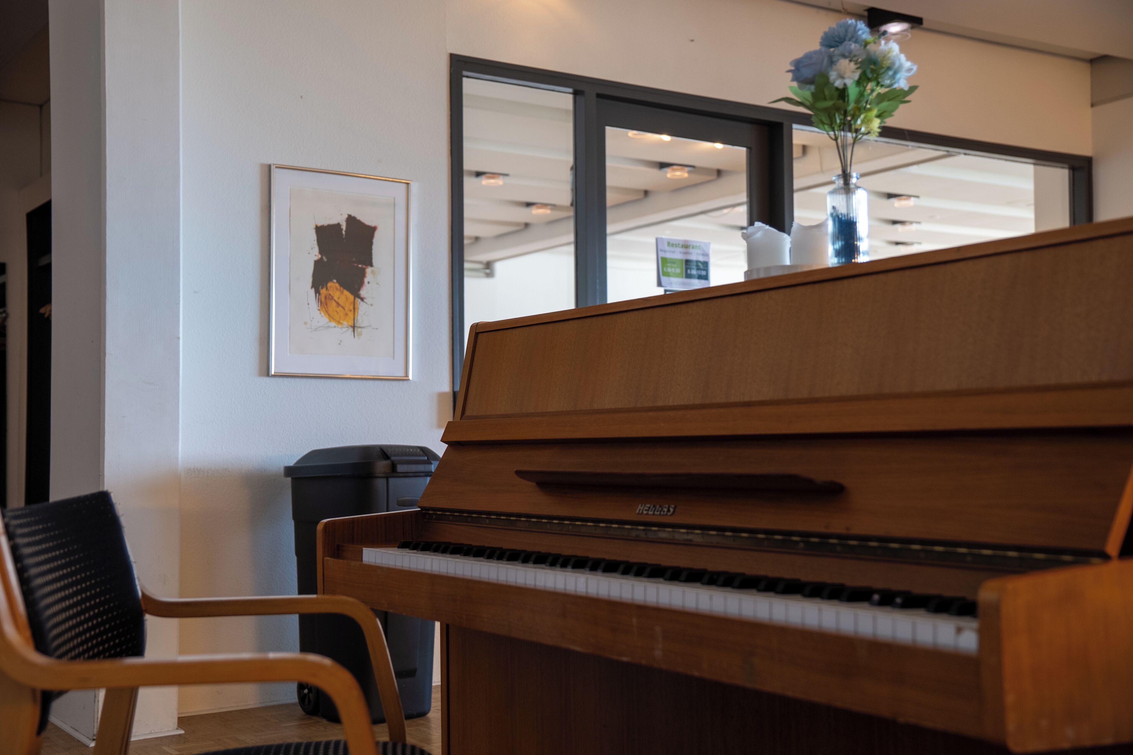 Um piano de cauda em um ambiente com uma janela ampla, uma obra de arte emoldurada na parede e uma cadeira.