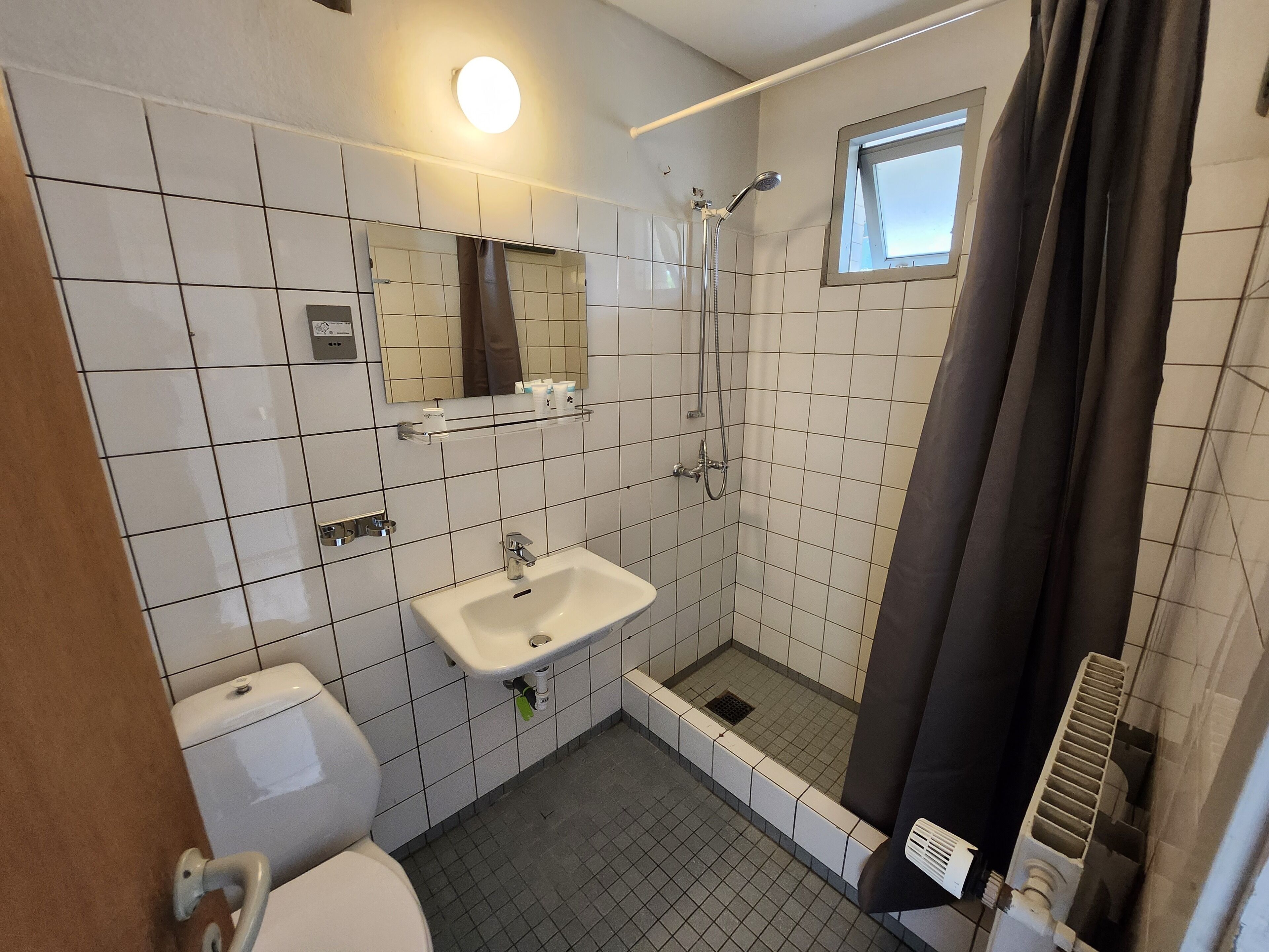 A bathroom with a toilet, sink, shower, and a small window.