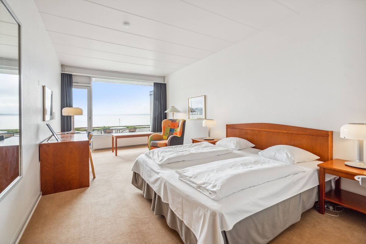 Habitación de hotel con una cama grande, un escritorio, una silla y vista al mar.