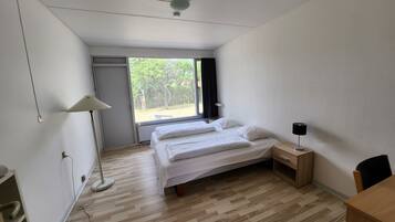 Ein Schlafzimmer mit Bett, Nachttisch, Lampe und Blick ins Freie.