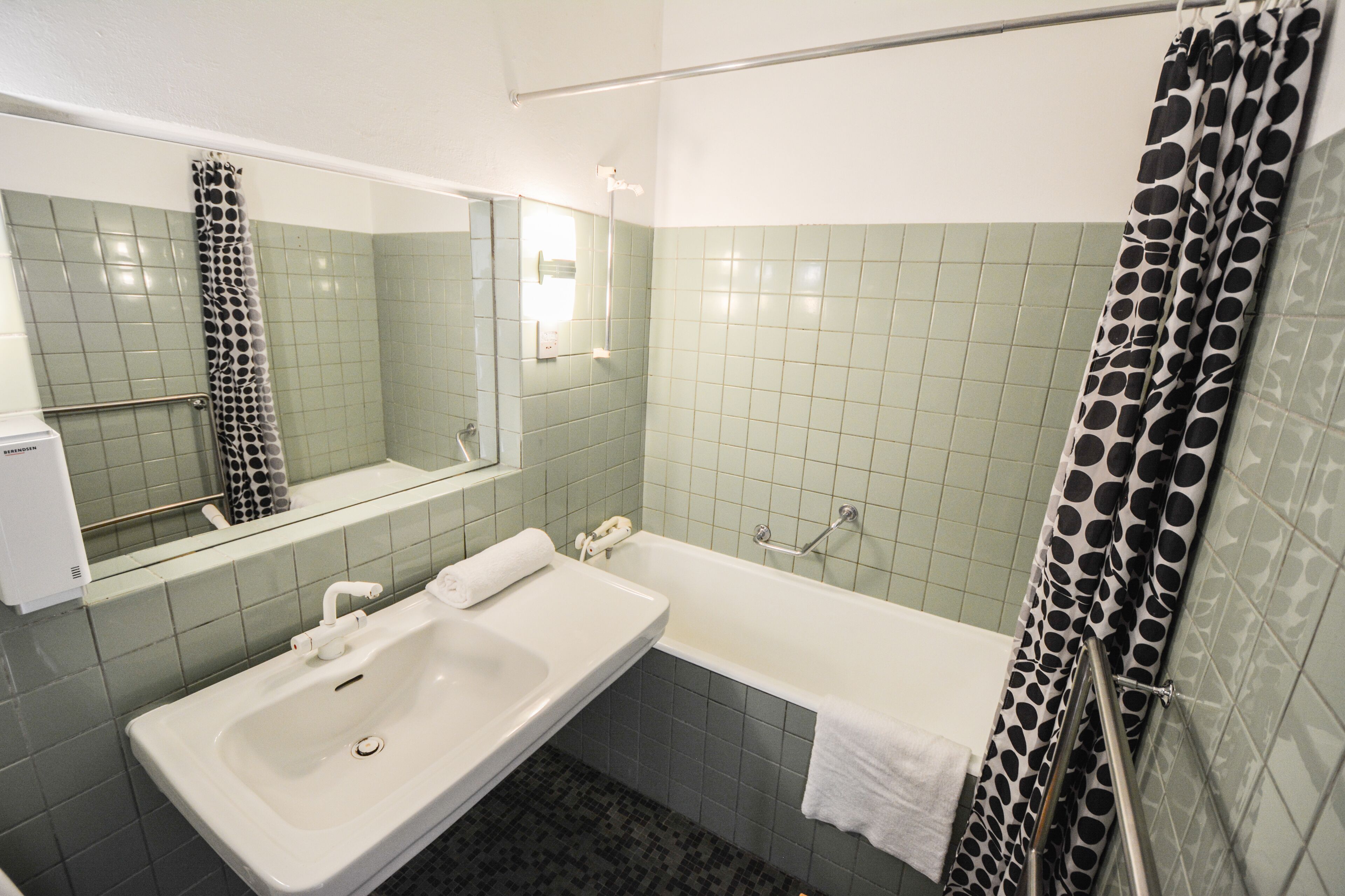 A bathroom with a sink, mirror, bathtub, and shower curtain.