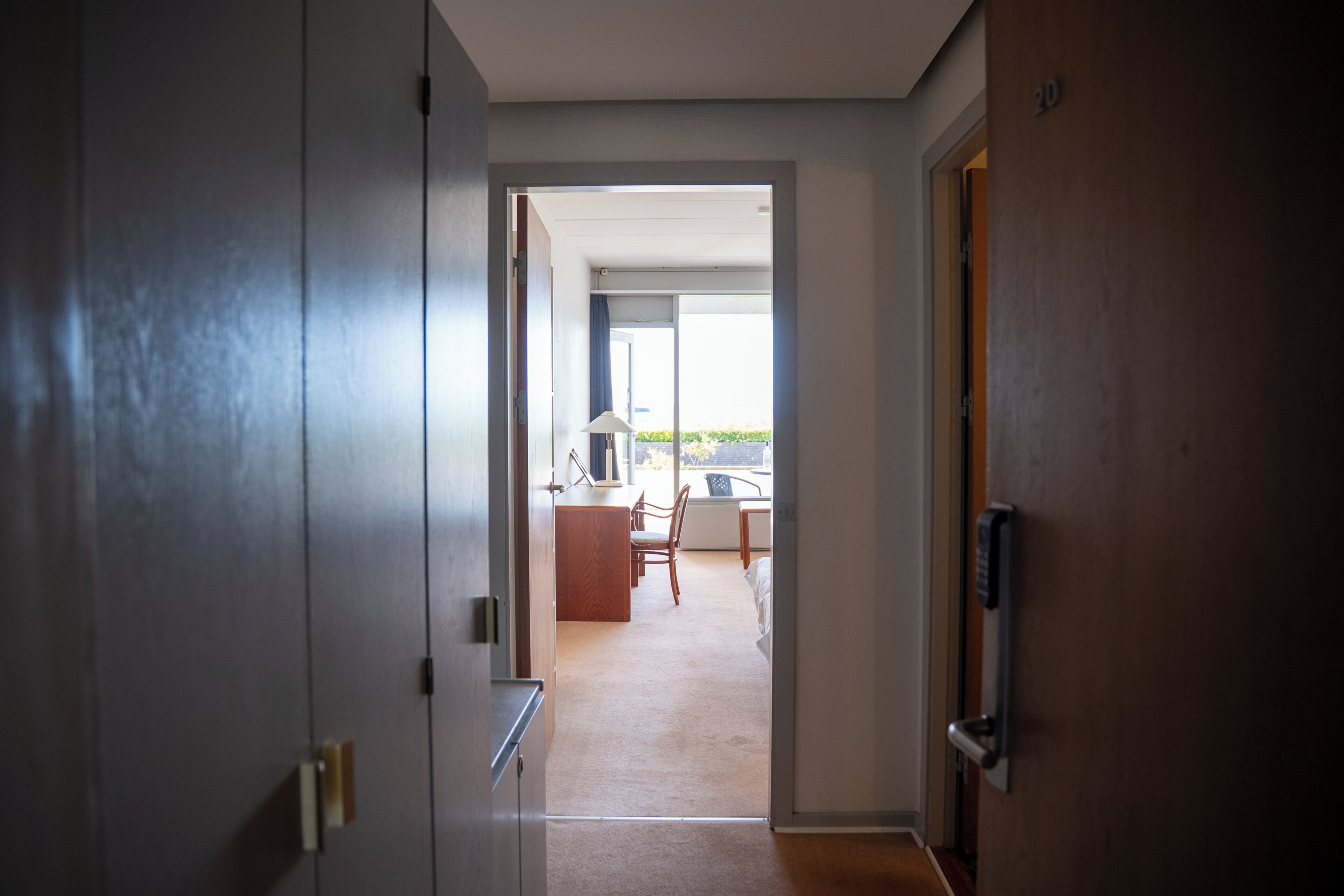 A hallway leading to a room with a desk, chair, and a view of the outdoors.