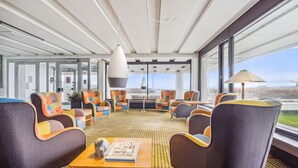 Un espacio lounge moderno con sillones coloridos, una mesa de centro de madera y ventanas amplias que ofrecen vistas al paisaje.