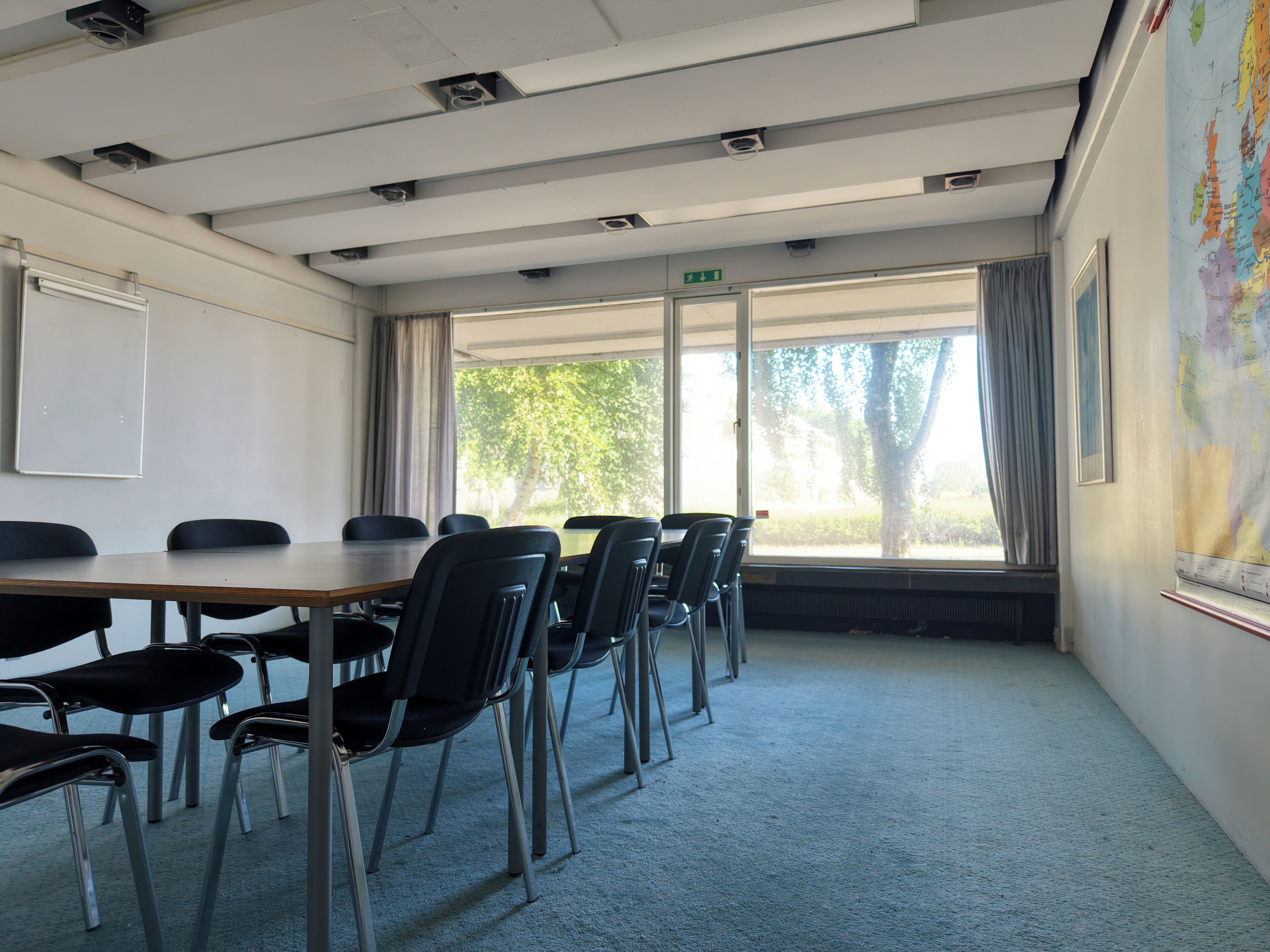 A conference room with a long table, chairs, a whiteboard, and a large window with curtains.