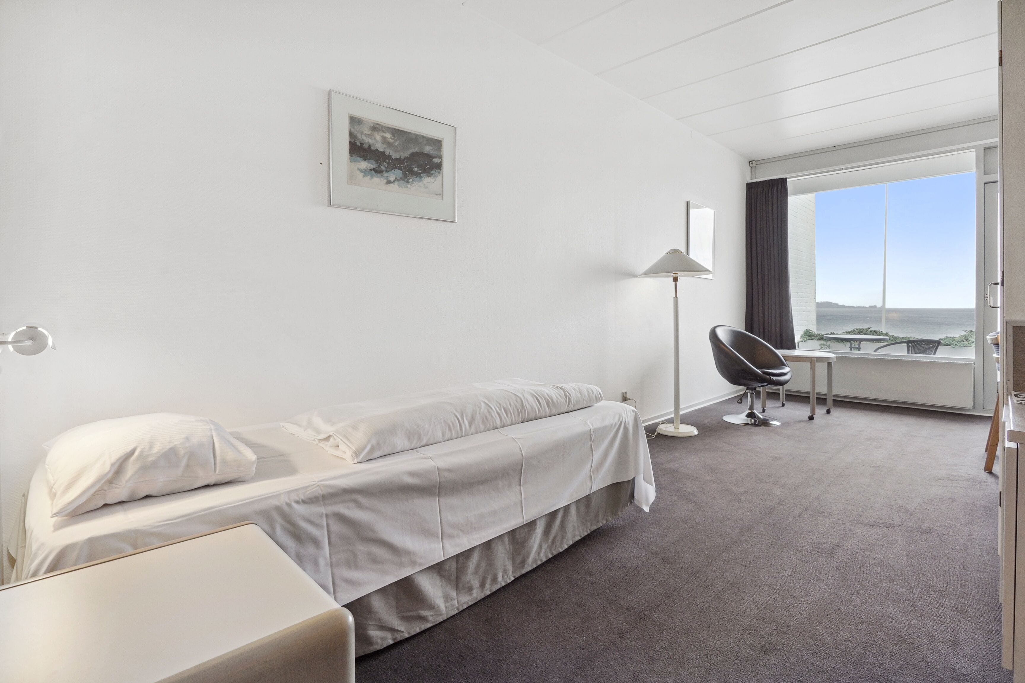 A hotel room with a bed, a desk, a chair, a lamp, and a large window with a view.