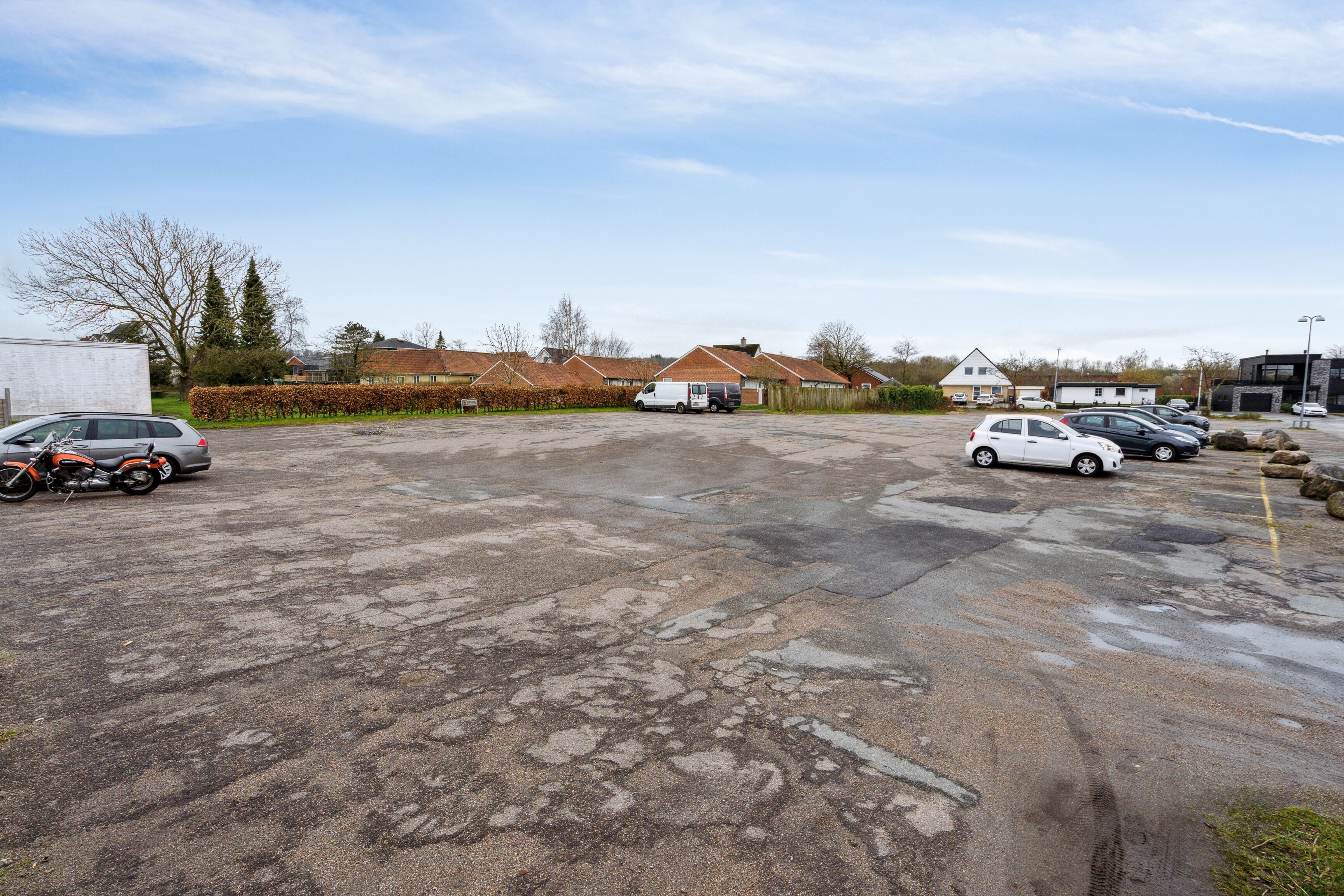 A parking lot with several cars and a motorcycle, surrounded by buildings and a clear sky.