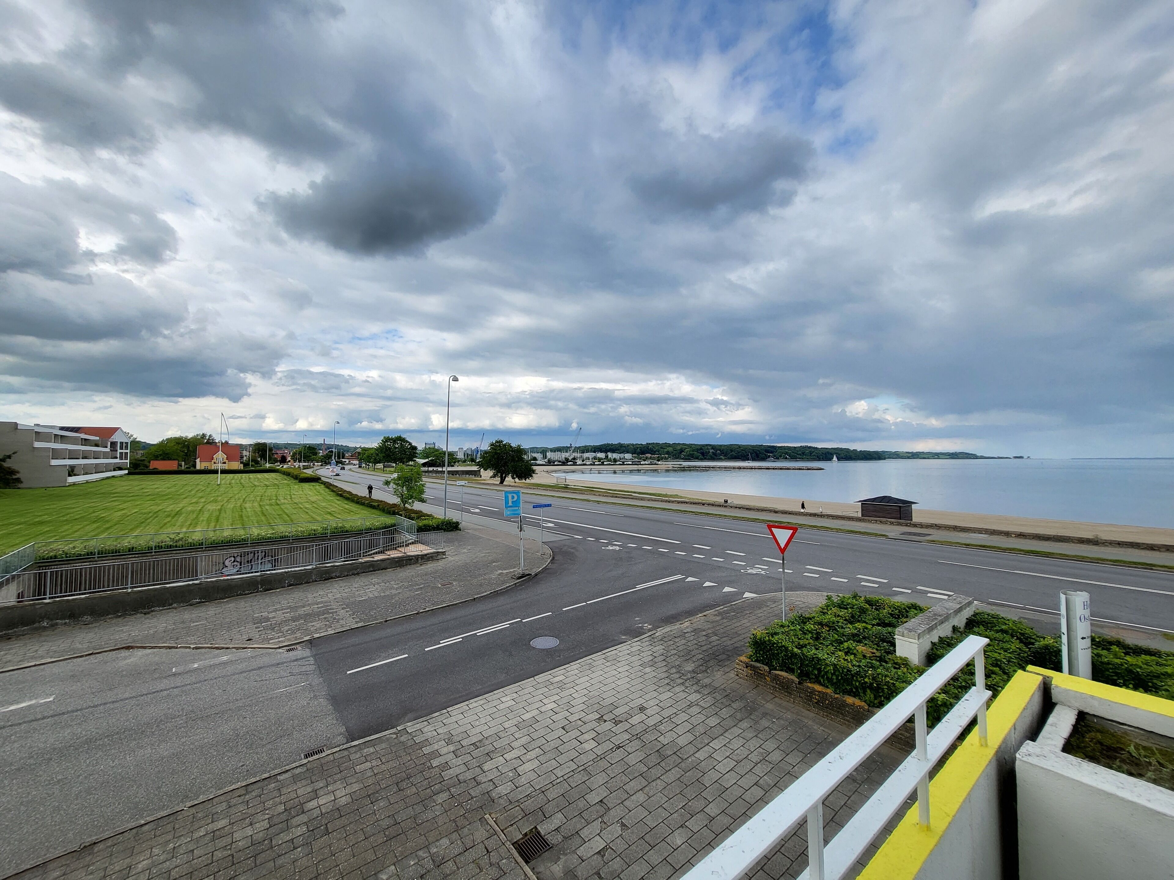 A coastal road with a pedestrian path, a parking sign, and a triangular warning sign.