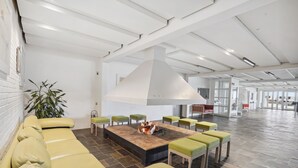 Un amplio salón con una chimenea central, asientos acolchados de color verde y un diseño de techo moderno.