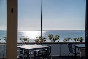 Una terraza con mesa y sillas, con vista al mar tranquilo y horizonte despejado.