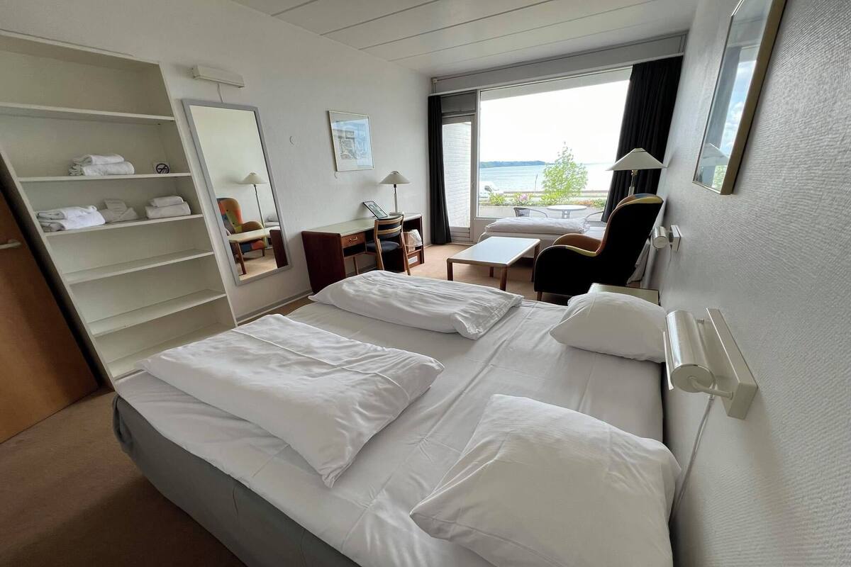 Habitación de hotel con dos camas, un escritorio, una silla, un armario y vista al mar.