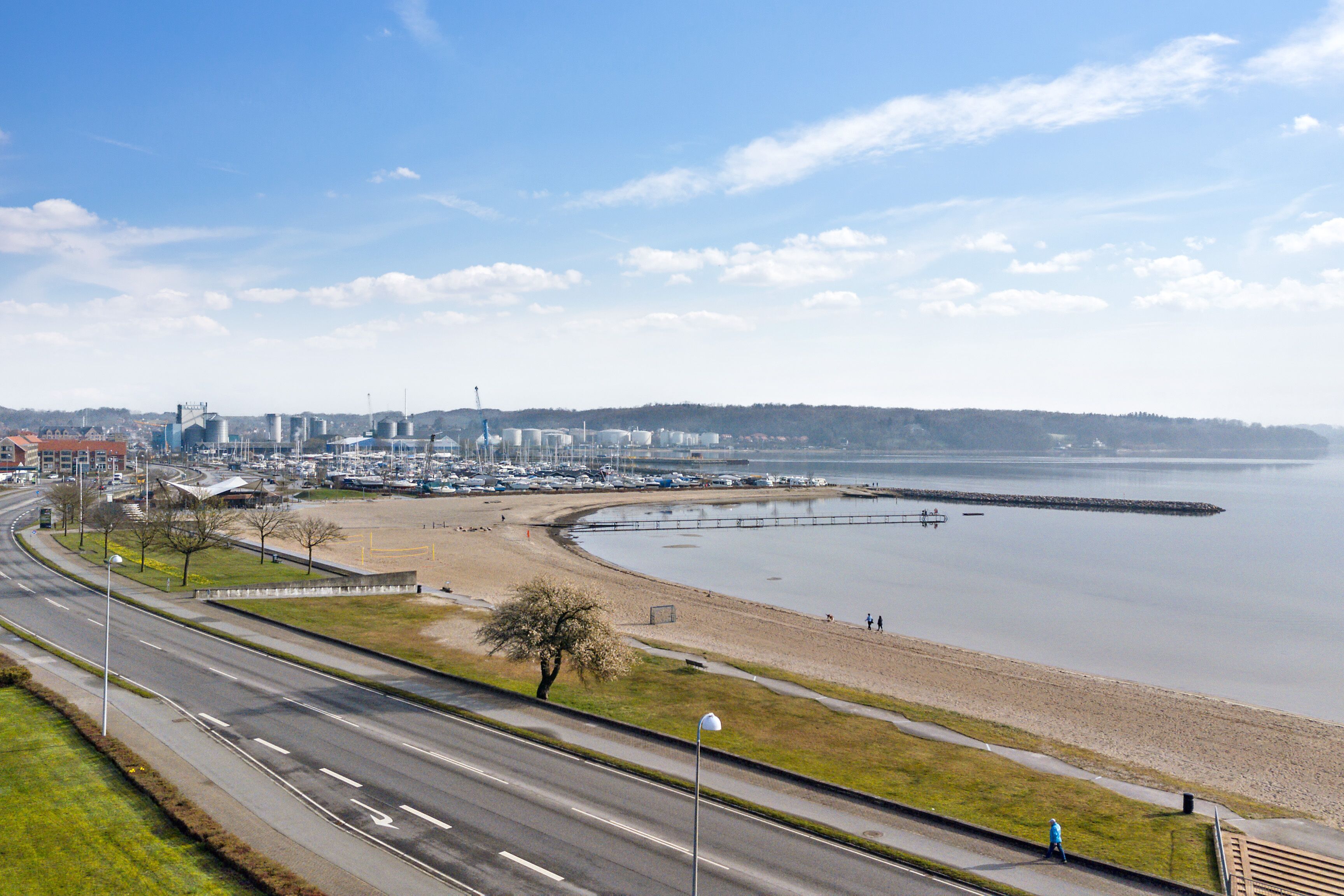Een kustweg met een strand en jachthaven op de achtergrond.