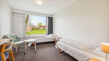 A hotel room with a bed, a chair, a small table, and a window with a view of the outdoors.