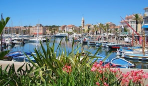 Un puerto deportivo con barcos amarrados, una torre de iglesia destacada y un cielo azul despejado.