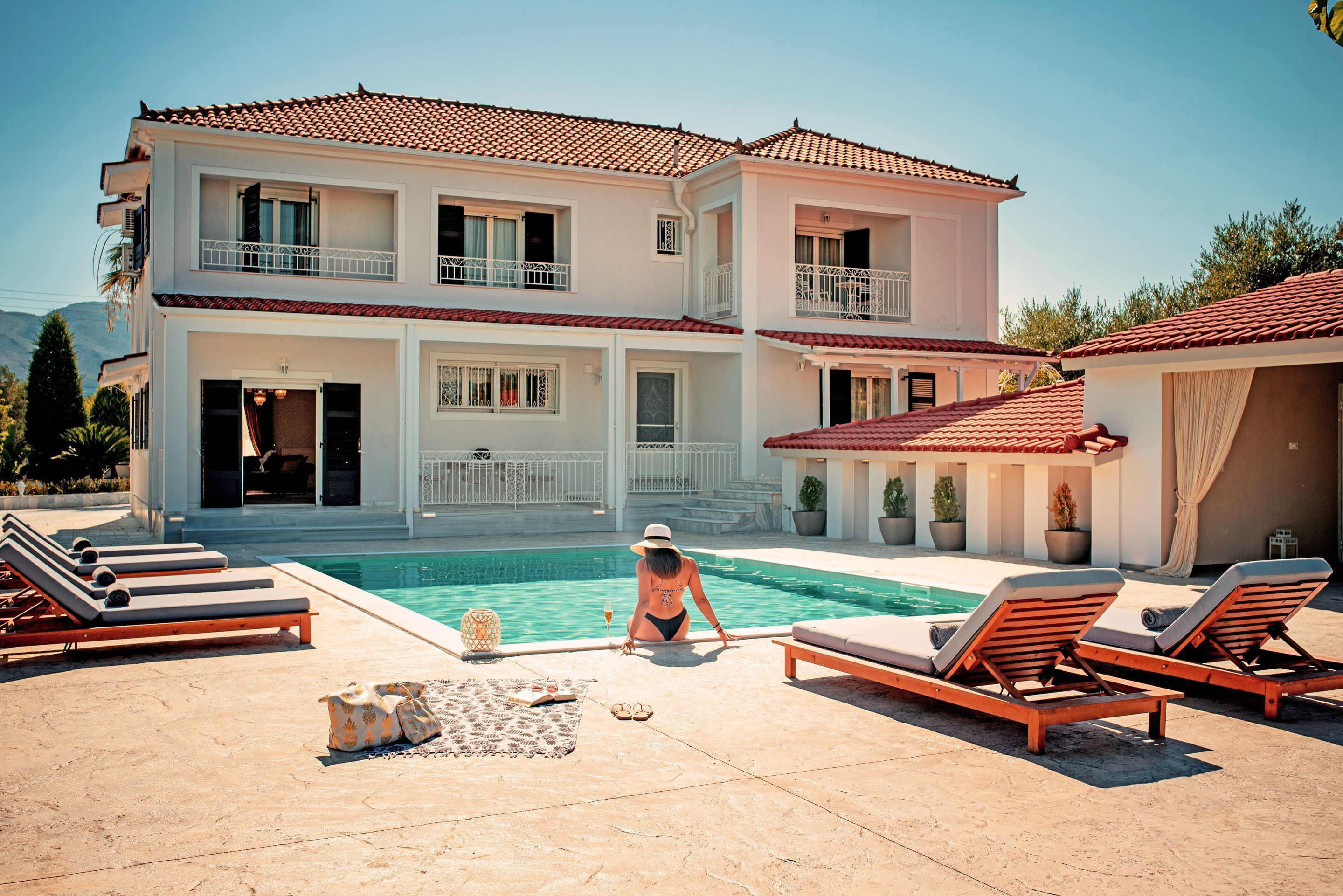 A two-story building with a swimming pool, lounge chairs, and potted plants.