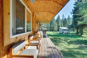 Une terrasse en bois avec des sièges et un barbecue, entourée d’une zone boisée.
