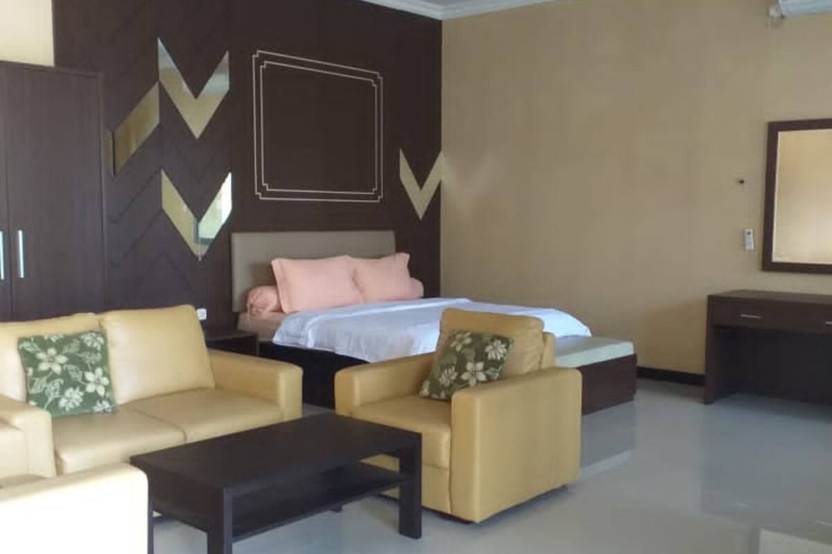 Quarto de hotel moderno com uma cama, dois sofás, uma mesa de centro e uma televisão.