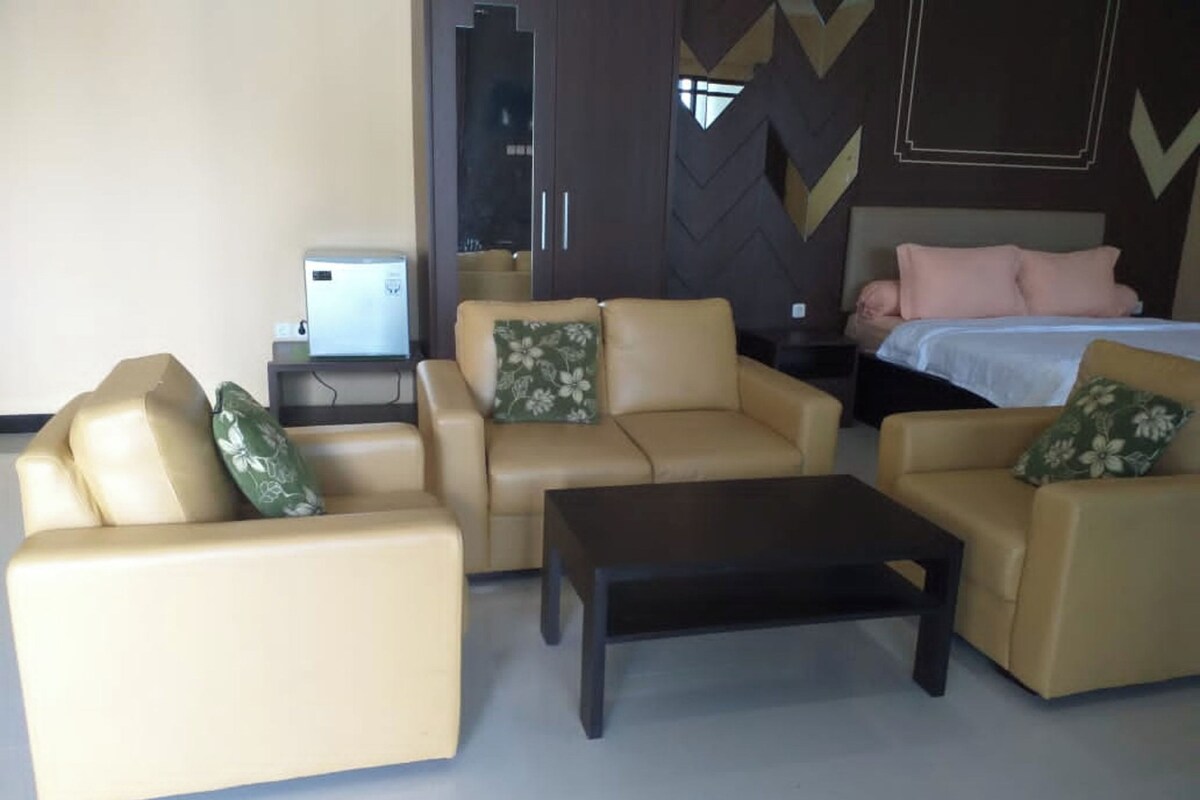 Habitación de hotel con un conjunto de sofá, una mesita de centro y una cama con colcha blanca y almohadas rosas.