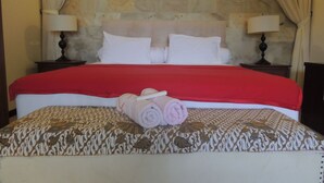 A neatly made bed with a red blanket, a patterned bedspread, and rolled towels on the bed. - Oase Van Java (Gedong)