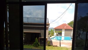 A view through a glass door of a residential area with a swimming pool, a two-story house, and a small tree. - Oase Van Java (Gedong)