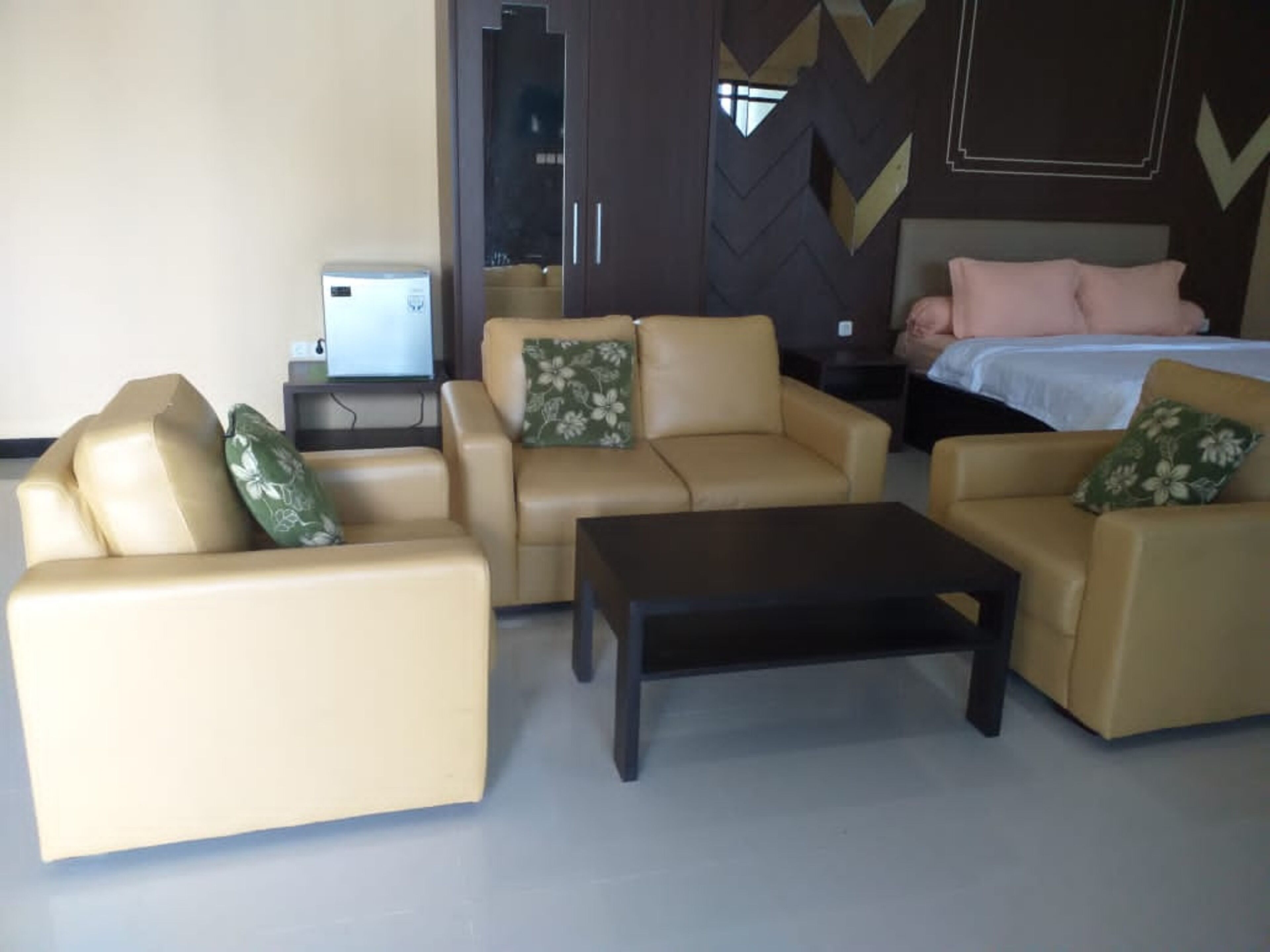 A hotel room with two beige sofas, a small table, a bed with a white bedspread and pink pillows, and a television on a stand.