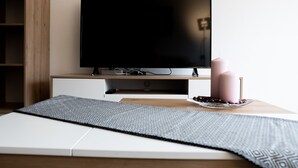 Una habitación moderna con un televisor de pantalla plana sobre un soporte de madera, una mesita con velas y fruta, y una alfombra estampada.