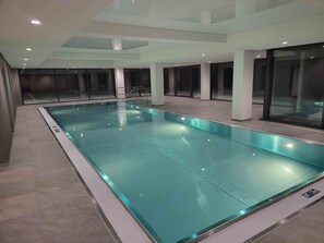 Une piscine intérieure à l’eau claire, dotée d’un sol carrelé et de murs en verre.
